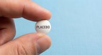Hand holding white placebo pill tablet between fingers against light blue background for medical research and pharmaceutical studies.