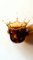 Golden tea splash creating crown shape in traditional glass cup with droplets frozen in motion against soft beige background for beverage advertising.