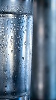 Clear glass bottle with fresh water droplets and condensation beads on transparent surface. Cool refreshing beverage container with moisture details.