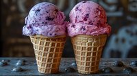 Creamy blueberry ice cream scoops in crispy waffle cones on rustic wooden surface, sweet frozen dessert with natural berry pieces and dark spots.