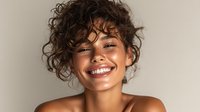 Young woman with curly hair and bright smile against neutral background, radiating confidence and joy in natural beauty portrait.