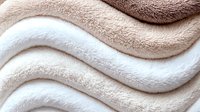 Soft wavy texture of plush fabric in beige and white tones creates gentle flowing lines and curves, showing luxurious textile surface with light and shadow play.