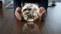 Businessman in dark suit holding illuminated globe showing world map and city lights on wooden desk, representing global business, international trade, and worldwide connectivity.