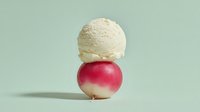 Vanilla ice cream scoop balanced on fresh red apple against soft green background creating playful food composition for healthy dessert concepts.