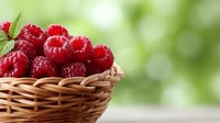 Fresh red raspberries in wicker basket on wooden table with green bokeh background for healthy eating and organic food concepts.