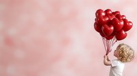 Blonde woman in white dress holding red heart balloons on pink bokeh background for romantic celebrations and Valentine's Day greeting cards.
