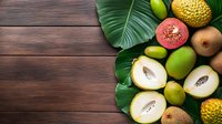 Fresh tropical fruits assortment with guava, kiwi and monstera leaves on dark wooden background. Copy space for menu, recipe or healthy eating concept.