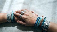 Hands wearing multiple silver rings and colorful woven bracelets in blue and brown tones, showcasing bohemian jewelry style and accessories fashion.