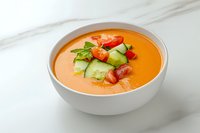 Fresh gazpacho soup garnished with cucumber, tomato and herbs served in white bowl on marble surface, cold summer appetizer for restaurant menu.