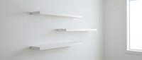 Modern white floating shelves mounted on clean wall in minimalist interior room with natural light from window for home organization and display.