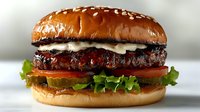 Juicy grilled burger with melted cheese, fresh tomato, crisp lettuce on sesame seed bun against light background, appetizing close-up shot for menu or advertising.
