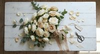 Wedding bouquet of cream and beige roses with eucalyptus on white wooden background. Bridal flowers arrangement with scattered petals and ribbon.