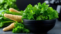 Fresh green parsley leaves in black ceramic bowl with raw parsnip roots on dark background, healthy cooking ingredients for vegetarian cuisine.