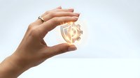 Female hand with medium skin tone holding glowing light bulb against white background, representing innovation, ideas, creativity, and business solutions for design and marketing projects.