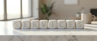 Wooden letter cubes spelling SERVICES on a marble surface in a bright modern office interior, representing business solutions and support.