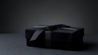 Luxury black gift box with black ribbon bow on dark surface, suitable for premium product packaging, branding mockups, and holiday promotional materials.