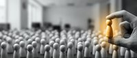Caucasian hand selecting golden leader figure from crowd of gray wooden pegs, representing recruitment, talent acquisition, and business leadership selection for corporate hiring needs.