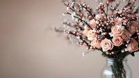 Delicate pink roses and white baby's breath arranged in clear glass vase against soft blurred background, creating romantic vintage mood for wedding and home decor styling.