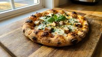 Freshly baked pizza with melted cheese, vegetables and herbs on wooden board near window with natural sunlight for food photography and restaurant menus.