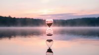 Hourglass floating on calm water surface at sunset with pink sky reflection, time concept for meditation and mindfulness practices.