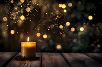 Glowing candle on rustic wooden table against dark background with magical golden bokeh lights creating cozy atmospheric holiday mood.