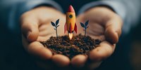 Hands holding soil with small rocket and plant seedlings, symbolizing business growth, startup launch, and nurturing new ventures.