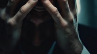 Stressed businessman holding head in hands showing mental exhaustion and workplace burnout in dark moody lighting for corporate wellness concepts.