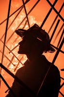 Silhouette of firefighter against intense orange flames and smoke background, dramatic profile view showing protective helmet and determined stance during emergency response.
