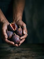 Farmer's hands holding fresh figs, one cut open showing interior. Dark background emphasizes organic produce. Suitable for food, agriculture, and culinary content.