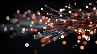 Glowing fiber optic strands emit orange and white light against dark background creating dynamic burst pattern with bokeh effect. For technology concepts.
