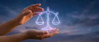 Human hands protecting glowing scales of justice symbol against twilight sky background representing legal protection and balanced judgment concepts.