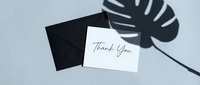 White thank you card with black envelope on light blue background, monstera leaf shadow, minimalist style for greeting and appreciation.