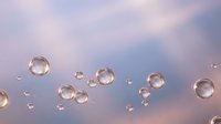 Transparent soap bubbles floating against soft pastel sky background with pink and blue gradient colors creating dreamy atmospheric scene.