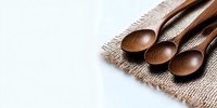 Rustic wooden spoons arranged on natural burlap fabric against white background, minimalist kitchen composition with copy space for menu or recipe design.