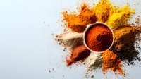 Vibrant spice powders scattered in sunburst pattern with bowl of paprika in center on white background, colorful cooking ingredients for food photography.