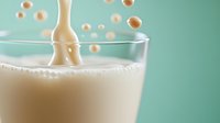 Splash of fresh milk or cream creating crown-shaped droplets in glass against mint green background, dynamic liquid motion photography with floating drops.