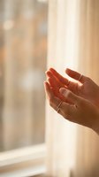 Open cupped hands reaching upward in warm sunlight streaming through window, symbolizing hope, prayer, spirituality and receiving blessings in peaceful moment.