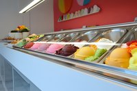 Colorful ice cream scoops displayed in modern gelato shop counter, featuring vibrant flavors from chocolate to fruit sorbets arranged in stainless steel containers.