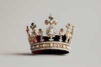 Ornate royal crown with pearl and crystal embellishments on velvet cushion against neutral background, featuring intricate gold metalwork and cross details.