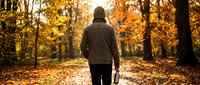 Man jogging on autumn forest path covered with golden fallen leaves, wearing dark athletic jacket, outdoor fitness and wellness activity.