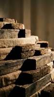 Stack of weathered wooden planks and lumber pieces with rough textured surfaces in warm natural lighting for construction and carpentry projects.
