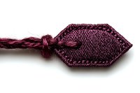 Burgundy silk decorative tassel with hexagonal top knot against white background, isolated macro shot showing intricate weaving pattern and textile details.
