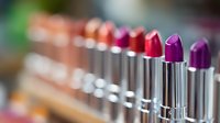 Row of colorful lipsticks in metallic tubes arranged in gradient from pink to purple shades, macro photography with selective focus and blurred background.