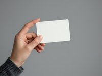 Hand holding blank white card against gray background, suitable for business branding, mockup designs, and promotional material presentations.