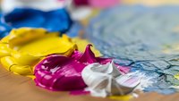 Colorful acrylic paint palette with yellow magenta white pigments mixed on wooden surface for artistic creative projects and painting techniques.