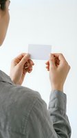 Person holding blank white card in hands, wearing gray shirt, isolated on white background for business card mockup, branding, and corporate identity design.