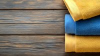 Rolled colorful bath towels on rustic wooden background with copy space. Soft cotton terry cloth in blue and yellow arranged on dark wood planks.