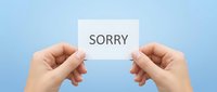 Hands holding white paper card with sorry text message against soft blue background for apology communication and forgiveness concepts.