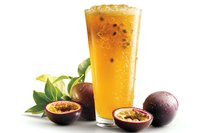 Refreshing passion fruit juice with ice in tall glass, surrounded by fresh cut passion fruits and green leaves on white background.