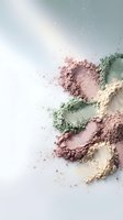 Colorful cosmetic powder scattered on white background creating artistic makeup composition with pink green and beige mineral pigments for beauty industry.